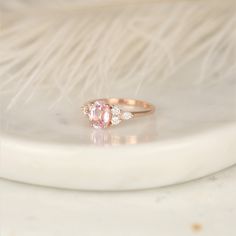 a pink diamond ring sitting on top of a white marble slab with feathers in the background