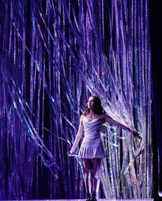 a woman standing in front of a purple curtain with streamers on it's sides