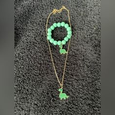 a green beaded necklace and bracelet with charms on it sitting on a gray carpet