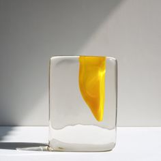 a yellow object in a glass vase on a white surface with sunlight coming through the window