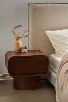 a bed with a wooden night stand next to it and a vase on the nightstand