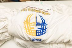 a white shirt with blue and yellow logos on it's chest, sitting on a table