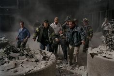 men walking through rubble with fire fighters in the background