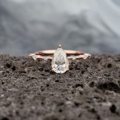 an engagement ring with a pear shaped diamond on top of it sitting on the ground