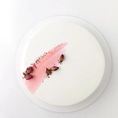 a white plate topped with a piece of cake covered in pink frosting and rose petals