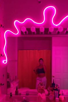 a woman standing in front of a bathroom mirror with pink lights on the walls and floor