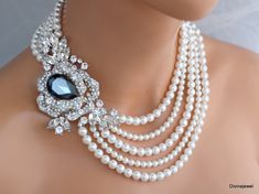 "This glamorous necklace has a dramatic brooch enhanced with a Montana teardrop, navettes, and Austrian pearls in your choice of color.  Brooch measures 4 1/4\" by 2 3/4\" at it widest point, and has a huge Austrian teardrop crystal 30 x 20 mm placed in the middle in Montana blue and clear rhinestones.  This multiple strand necklace measures 17 1/2\" long inner strand.  Pearls measure 8 and 6 mm.  Finished off with a five strand tube clasp for a very secure hold! Please choose desired pearl colo Crystal Pearl Necklace With Rhinestones For Wedding, White Rhinestone Necklace With Pearl Chain For Wedding, Pearl White Rhinestone Necklace For Wedding, Exquisite Pearl Wedding Necklace, Wedding Rhinestone Necklace With Pearl Chain, Elegant Pearl Necklace With Rhinestones For Wedding, Wedding Pearl Necklace With Rhinestones, Elegant Pearl Bridal Necklace With Jewels, Glamorous Silver Pearl Necklace For Wedding