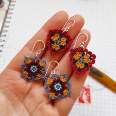 the hand is holding three small crocheted earrings in different colors and designs on them