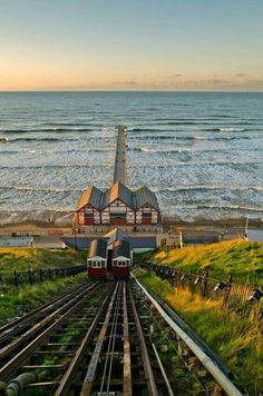 two trains are on the tracks next to the beach and ocean in front of them