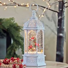 a white lantern with red flowers and lights on it sitting on a table next to other decorations