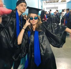 two people in graduation caps and gowns posing for the camera with their hands up