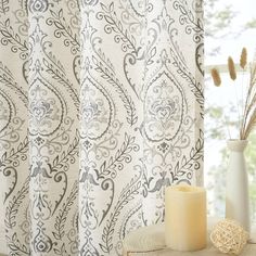 a white vase sitting on top of a wooden table next to a window covered in curtains