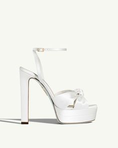 Contemporary elegance. Our Cupid Plateau Sandal combines a sturdy plateau and sky-high heel with delicate ankle straps and a refined knot motif that decorates the tip of the foot. This open-toe style is entirely Made in Italy from silky white satin. Wedding Heels For Bride Long Dress, Bridal Platform Shoes, Platform Bridal Heels, Luxury Ankle Tie Sandals For Formal Occasions, Designer Wedding Platform Heels, Plateau Shoes, Aquazurra Heels, White Platform Heels, Wedding Guest Bags