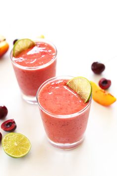 two glasses filled with fruit and garnish on top of a table