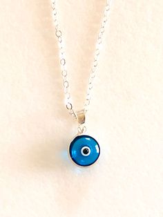 "Darling petite translucent London Blue evil eye charm on delicate sterling necklace. Handmade in Turkey this darling little two-sided translucent glass evil eye is only 3/8\" with sterling silver rim and bail. The beautiful London Blue color makes it even more striking. Petite charm hangs from delicate .925 sterling silver cable chain with spring ring clasp. Total drop with bail is 5/8\"." Paris Charm Bracelet, Paris Souvenirs, Hamsa Jewelry, Sterling Necklace, Beautiful London, Translucent Glass, Sterling Necklaces, Blue Evil Eye, Gifts For An Artist