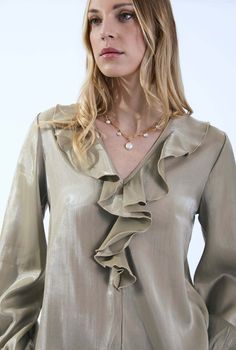 Crafted from a lightweight and flowy satin, this James Lakeland blouse exudes elegance. The luxurious sheen adds a touch of sophistication, making it ideal for various occasions. The V-neck features dramatic ruffling, creating a focal point that draws attention to the neckline. It’s a statement detail that elevates the overall design. The two long bell sleeves add a romantic flair. They end in elasticated cuffs, allowing for comfort and ease of movement. The slight ruching at the shoulders adds Formal V-neck Blouse With Ruffles, Elegant V-neck Ruffled Blouse, Elegant Gold Blouse For Workwear, Elegant Gold Blouse For Work, Elegant Ruffled V-neck Blouse, Elegant V-neck Ruffle Blouse, Gold V-neck Blouse For Work, Elegant Gold Silk Blouse, Chic Gold Formal Blouse