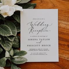 the wedding reception card is surrounded by greenery and white flowers on a wooden table