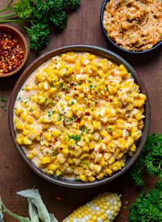 a bowl filled with corn next to two bowls of dip and some parsley on the side