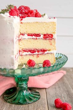 a cake with white frosting and raspberries is on a green glass plate