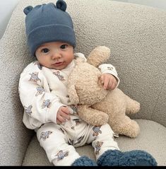 a baby sitting on a couch holding a teddy bear