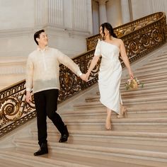 a man and woman holding hands while walking up some stairs