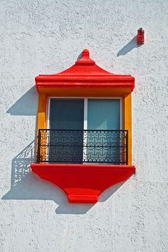 a red and yellow window on the side of a white building with a balconi