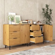 a wooden cabinet with drawers and pictures on top in a room next to a potted plant