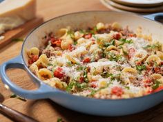 a skillet filled with pasta and meat on top of a wooden table next to bread