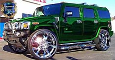 a green hummer truck parked in front of a building with chrome wheels and rims