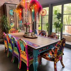 a dining room table with colorful chairs and decorations on the top, in front of large windows