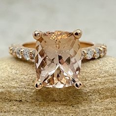 an engagement ring with a cushion cut peach morganite surrounded by diamond accents on a rock