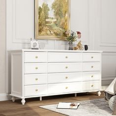 a white dresser sitting in a living room next to a painting