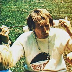 two people sitting in the grass with one holding a cell phone to his ear and another listening to headphones