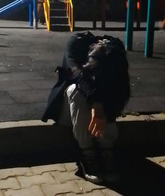 a person sitting on the ground with their head in his hands, near a playground