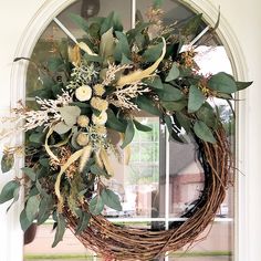 a wreath on the front door with flowers and greenery hanging from it's side