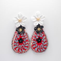 pair of red and white earrings with flowers on top of each earring, against a white background