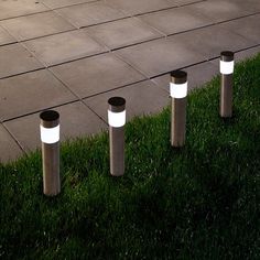 four lights that are sitting in the grass near each other on some concrete slabs and one is lit up