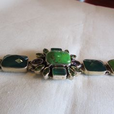 "Sterling silver link bracelet with two amethyst faceted stones and various green stones. There are dark green cushion cut stones, lime green cabs, and two colors of faceted small marquis stones. Some look like peridot. Stamped IB India 925. The center cluster is 1\" tall x 1 1/8\" wide. The length of the bracelet is 8\". Lobster claw clasp. Good condition. Shipped by US mail. LB-1" Modern Green Jewelry With Gemstone Accents, Unique Faceted Green Jewelry, Modern Green Gemstone Bracelets, Unique Green Faceted Jewelry, Modern Green Peridot Jewelry, Unique Green Gemstone Bracelets, Green Gemstone Bracelets, Green Peridot Multi-stone Jewelry, Green Multi-stone Bracelets For Gifts