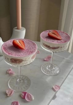 two desserts with strawberries are sitting on a table next to a vase and candle