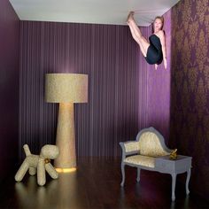 a woman is hanging upside down on the wall next to a chair and lamp in a room with purple walls