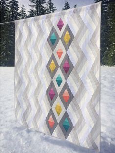 a quilted wall hanging in the snow with trees in the backgroung