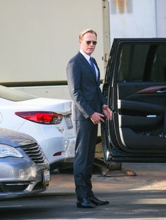 a man in a suit and sunglasses standing next to a car with the door open