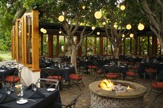 an outdoor dining area with tables, chairs and fire pit in the center surrounded by trees