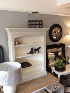 a living room filled with furniture next to a wall mounted mirror and lamp on top of a wooden table