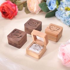 three wooden boxes with wedding rings in them on a table next to some pink flowers