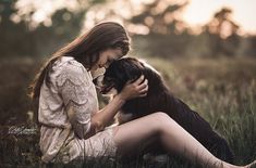 a woman is sitting in the grass with her dog and petting it's face