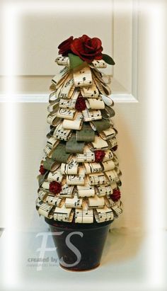 a small christmas tree made out of old sheet music sheets and roses sits in front of a door