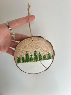 a hand holding a small wooden ornament with trees painted on it's side