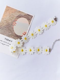 a white bracelet with yellow and white daisies attached to it, next to a card