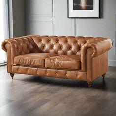 a tan leather couch sitting on top of a wooden floor next to a painting hanging on the wall